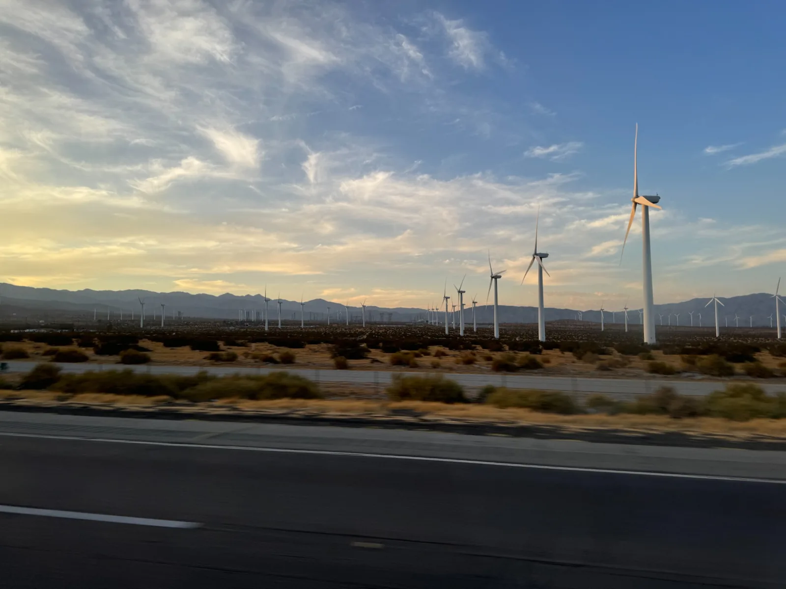 夕方の空の下に多数の風力発電機が並ぶ帰路の景色