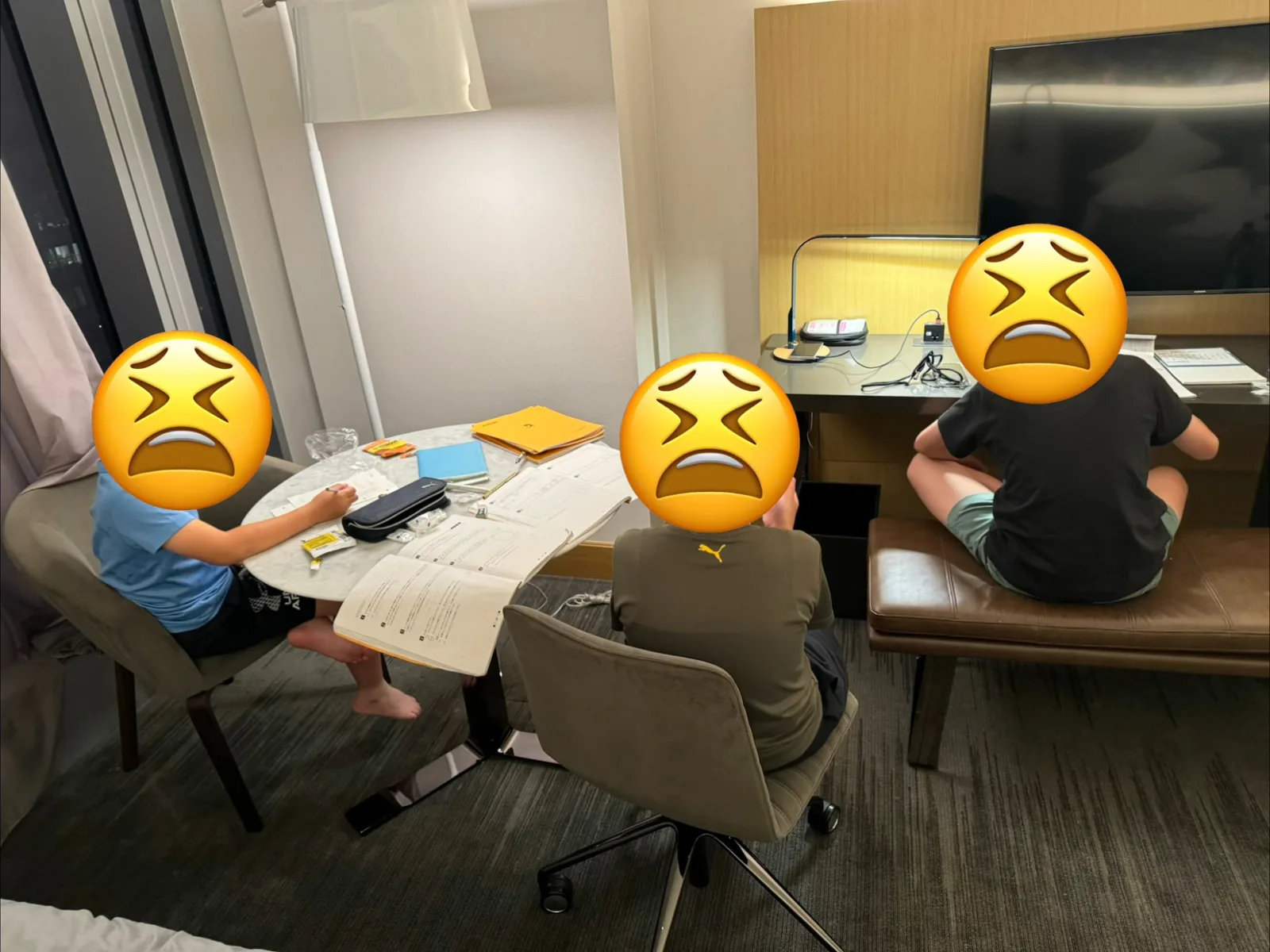ホテルの部屋で教材を広げて勉強する3人の子ども
